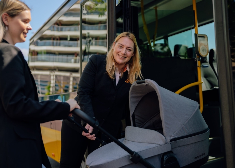 Chauffeuse helpt vrouw met kinderwagen de bus in